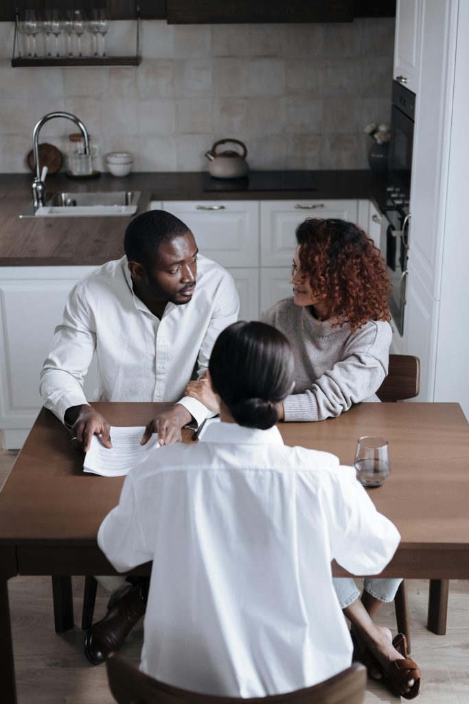 Three adults discussing documents at a table in a modern kitchen.